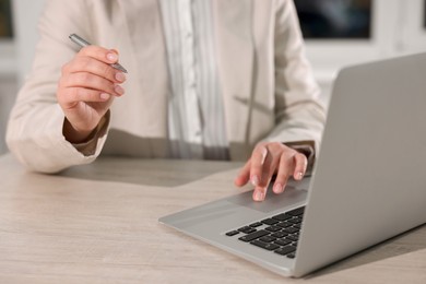 Woman with pen working on laptop at wooden table, closeup. Electronic document management