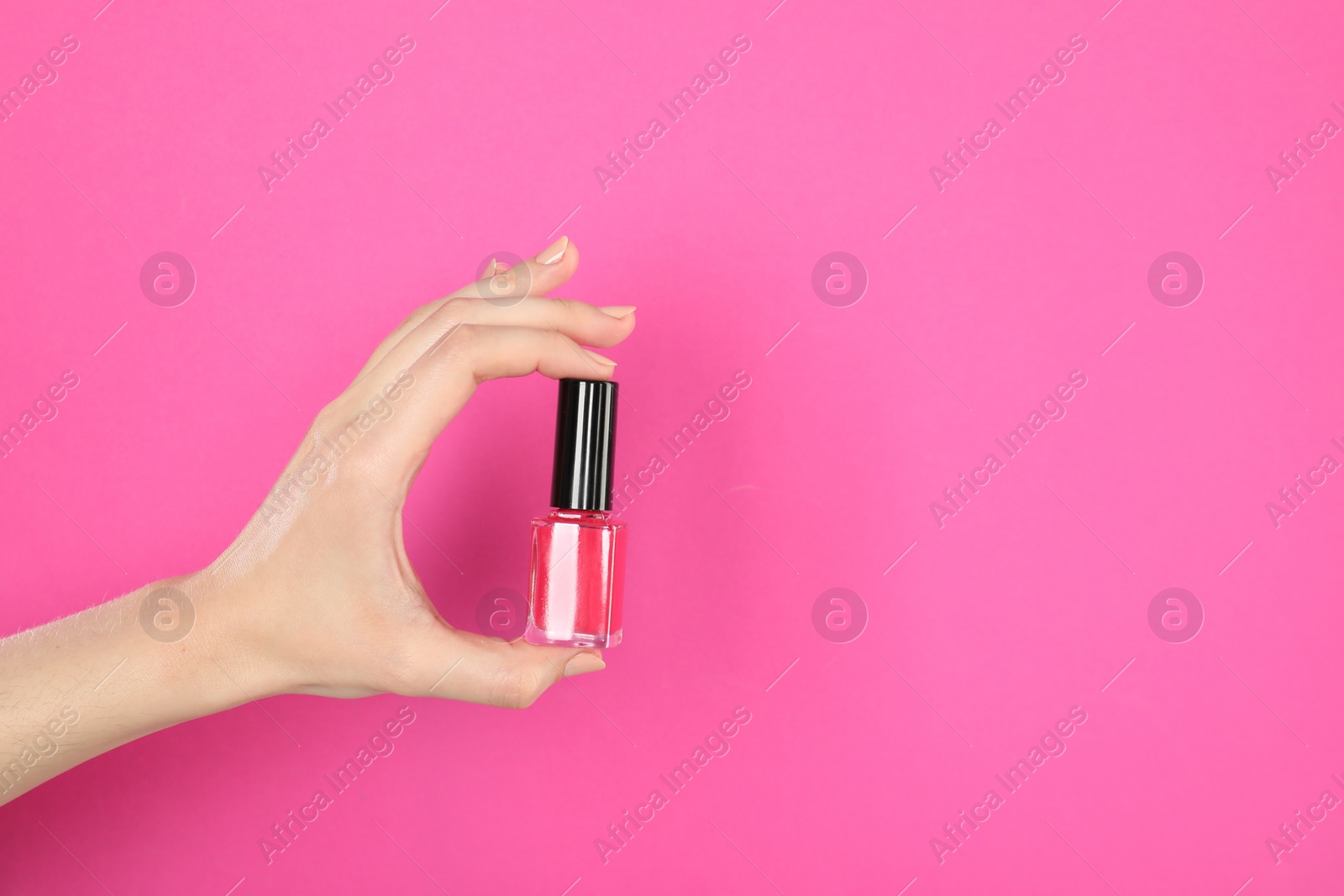 Photo of Woman holding nail polish on pink background, closeup. Space for text