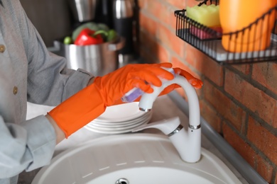 Photo of Young woman cleaning tap in kitchen