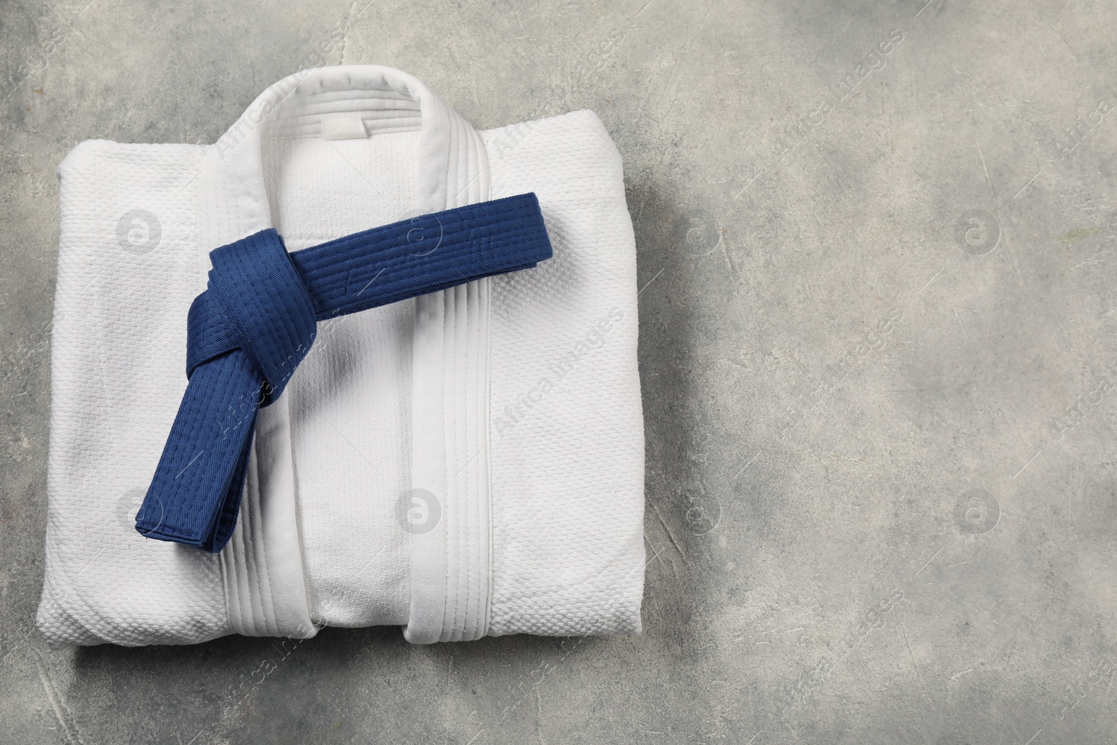 Photo of Blue karate belt and white kimono on gray textured background, top view. Space for text