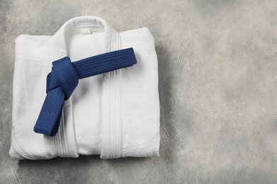 Blue karate belt and white kimono on gray textured background, top view. Space for text