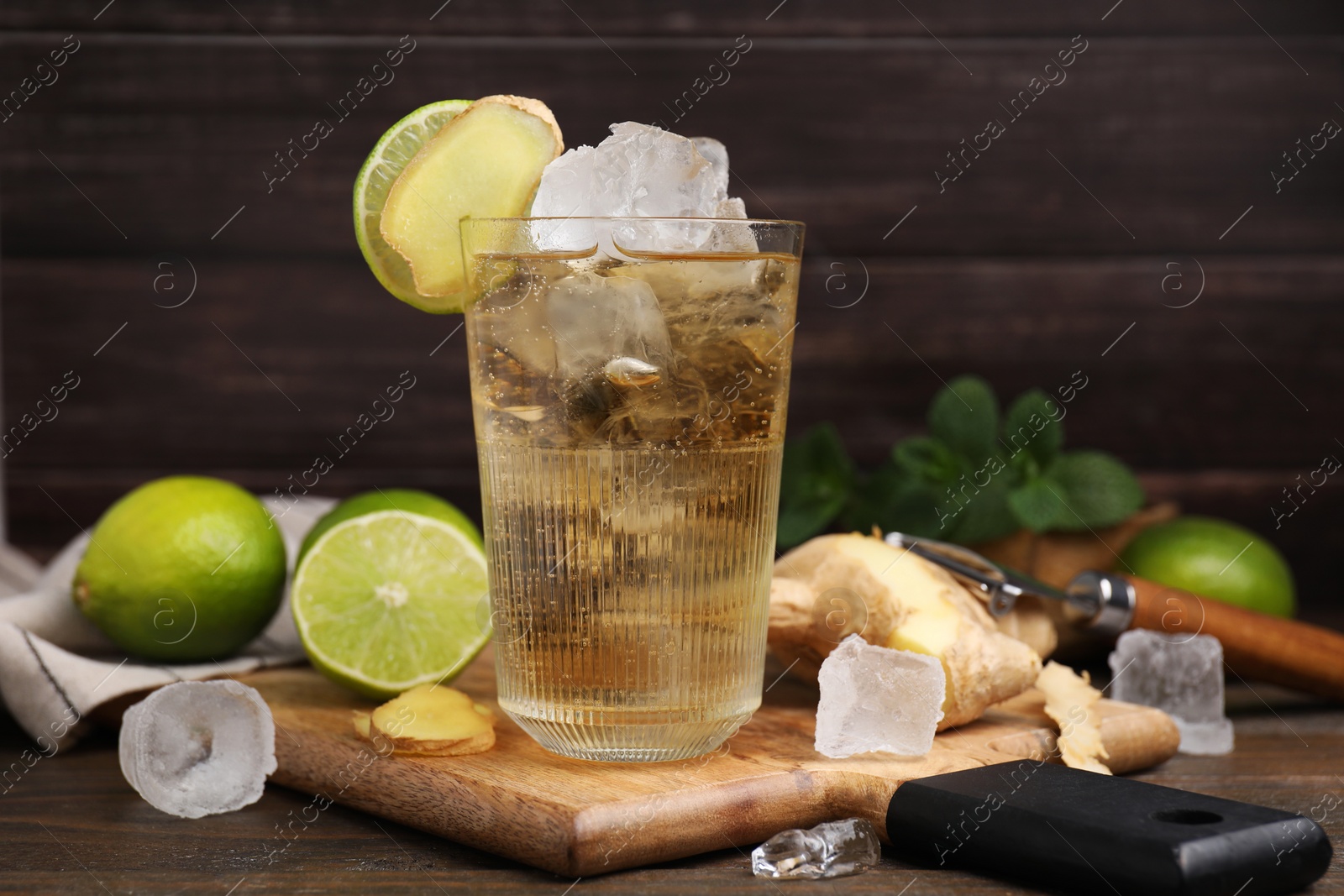 Photo of Glass of tasty ginger ale with ice cubes and ingredients on wooden table