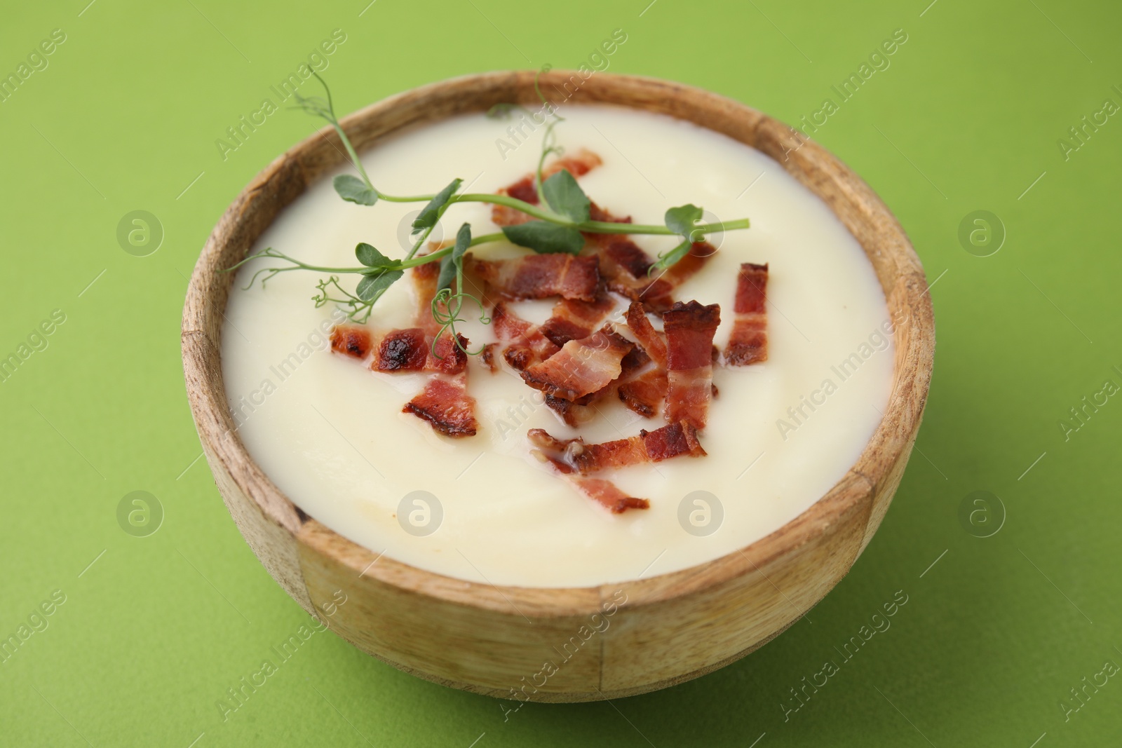 Photo of Delicious potato soup with bacon and microgreens in bowl on green table, closeup