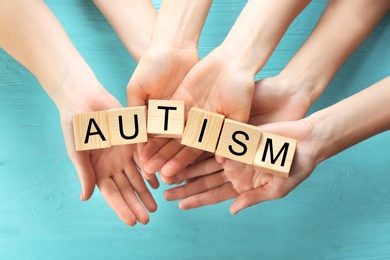 Group of people holding cubes with word "Autism" on wooden background