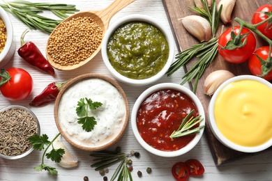 Flat lay composition with different sauces and ingredients on white wooden background