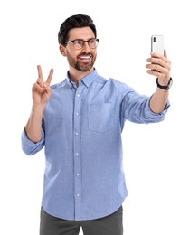 Photo of Smiling man taking selfie with smartphone and showing peace sign on white background