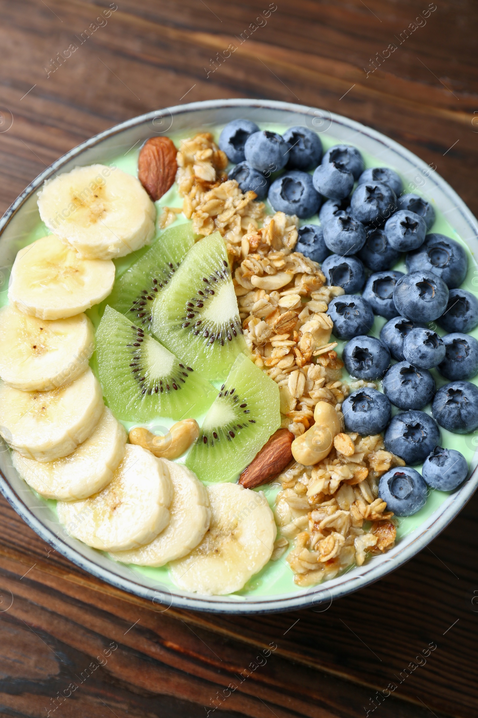 Photo of Tasty smoothie bowl with fresh fruits and oatmeal on wooden table, above view