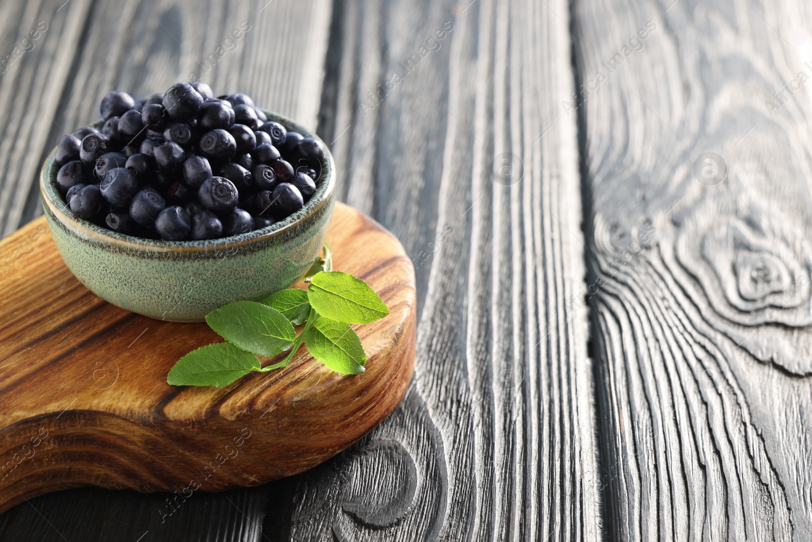 Photo of Bowl of tasty fresh bilberries and green leaves on wooden table. Space for text