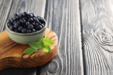 Photo of Bowl of tasty fresh bilberries and green leaves on wooden table. Space for text