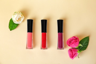 Lip glosses and flowers on color background