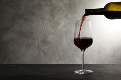Pouring red wine from bottle into glass on table. Space for text
