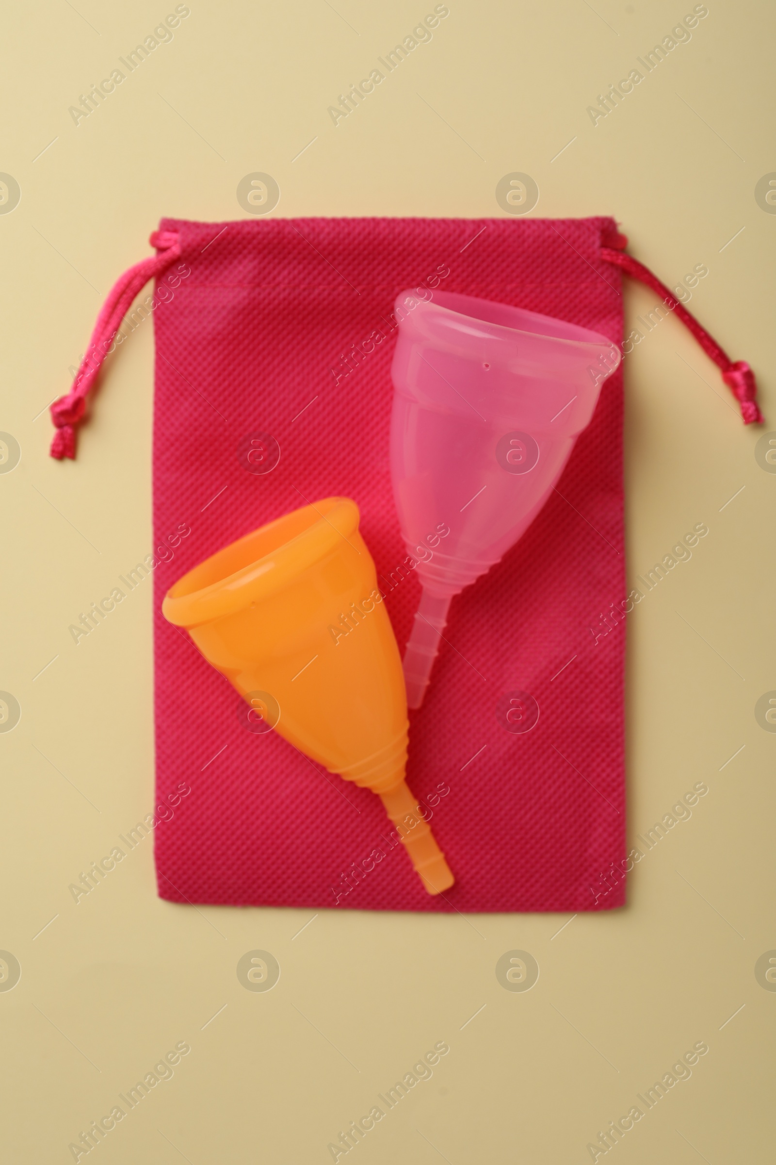 Photo of Menstrual cups with cotton bag on beige background, top view