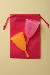 Menstrual cups with cotton bag on beige background, top view