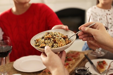 Photo of Man giving bowl of traditional Christmas kutia to woman at festive dinner indoors, closeup. Slavic dish