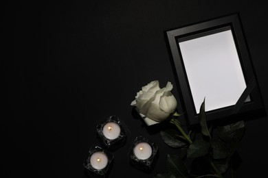 Funeral photo frame with black ribbon, white rose and candles on dark background, flat lay. Space for text