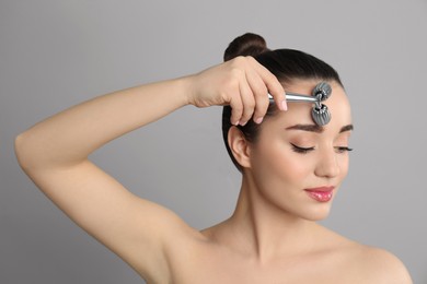 Photo of Woman using metal face roller on grey background