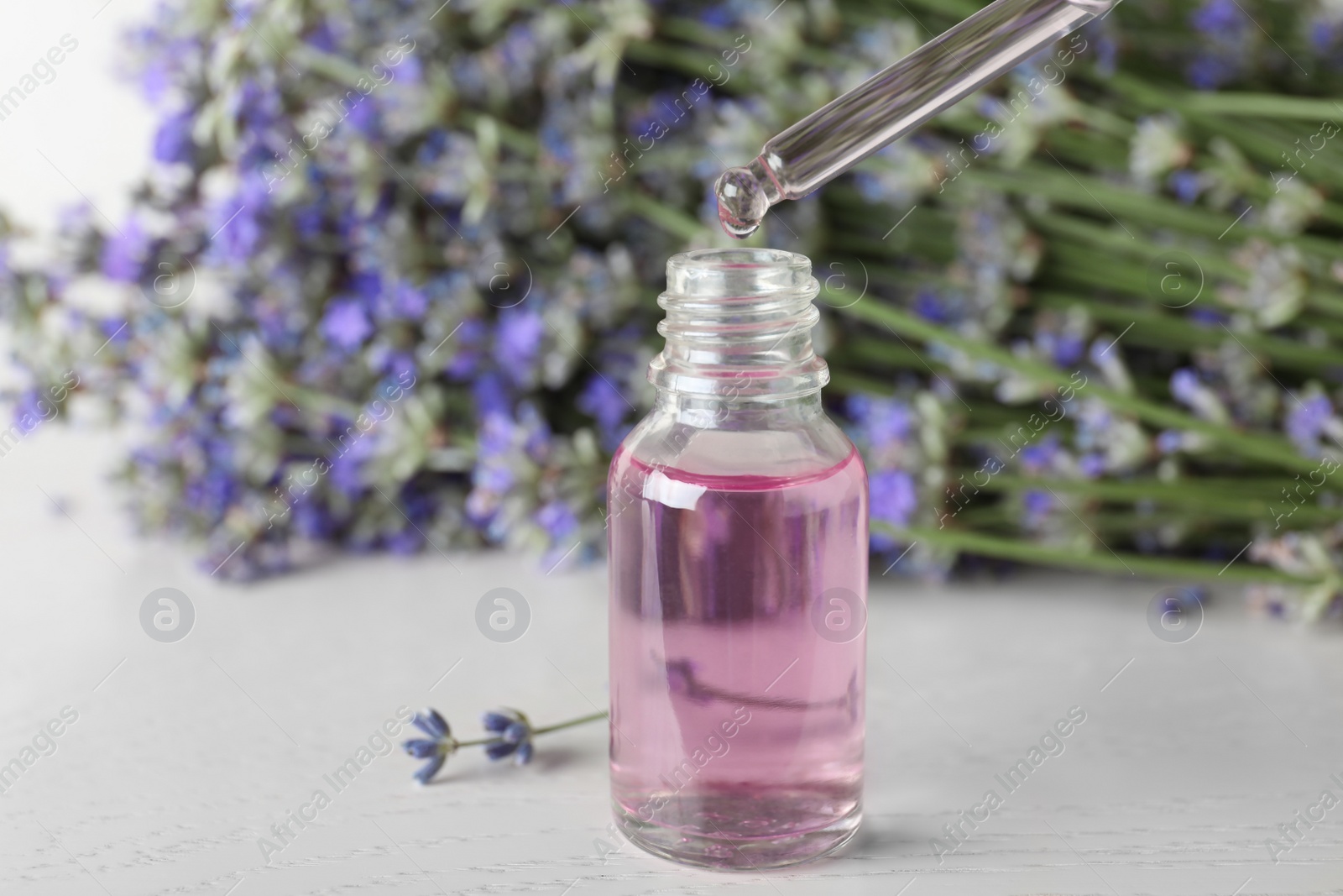 Photo of Dripping essential oil into bottle near lavender flowers on white wooden table