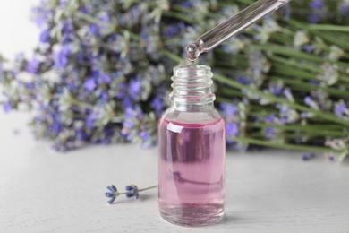 Dripping essential oil into bottle near lavender flowers on white wooden table