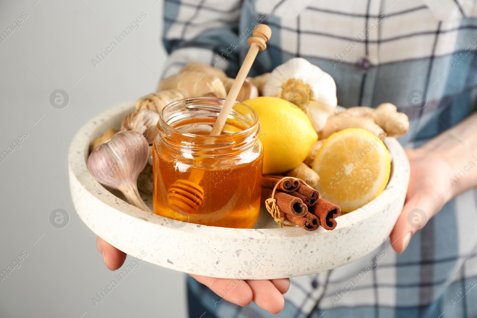 Photo of Woman holding tray with fresh products on grey background, closeup. Natural antibiotics