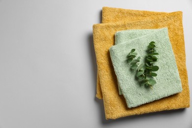 Soft folded towels with eucalyptus branches on light grey background, top view. Space for text