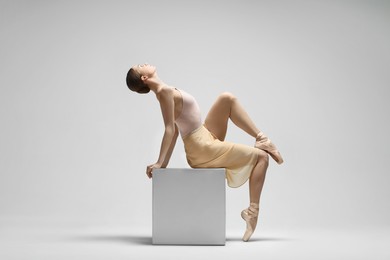 Young ballerina practicing dance moves on cube against white background