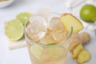 Photo of Glass of tasty ale with ice cubes, lime and ginger slices on blurred background, closeup