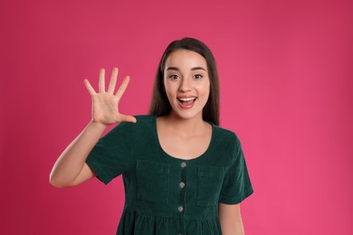 Photo of Woman showing number five with her hand on pink background