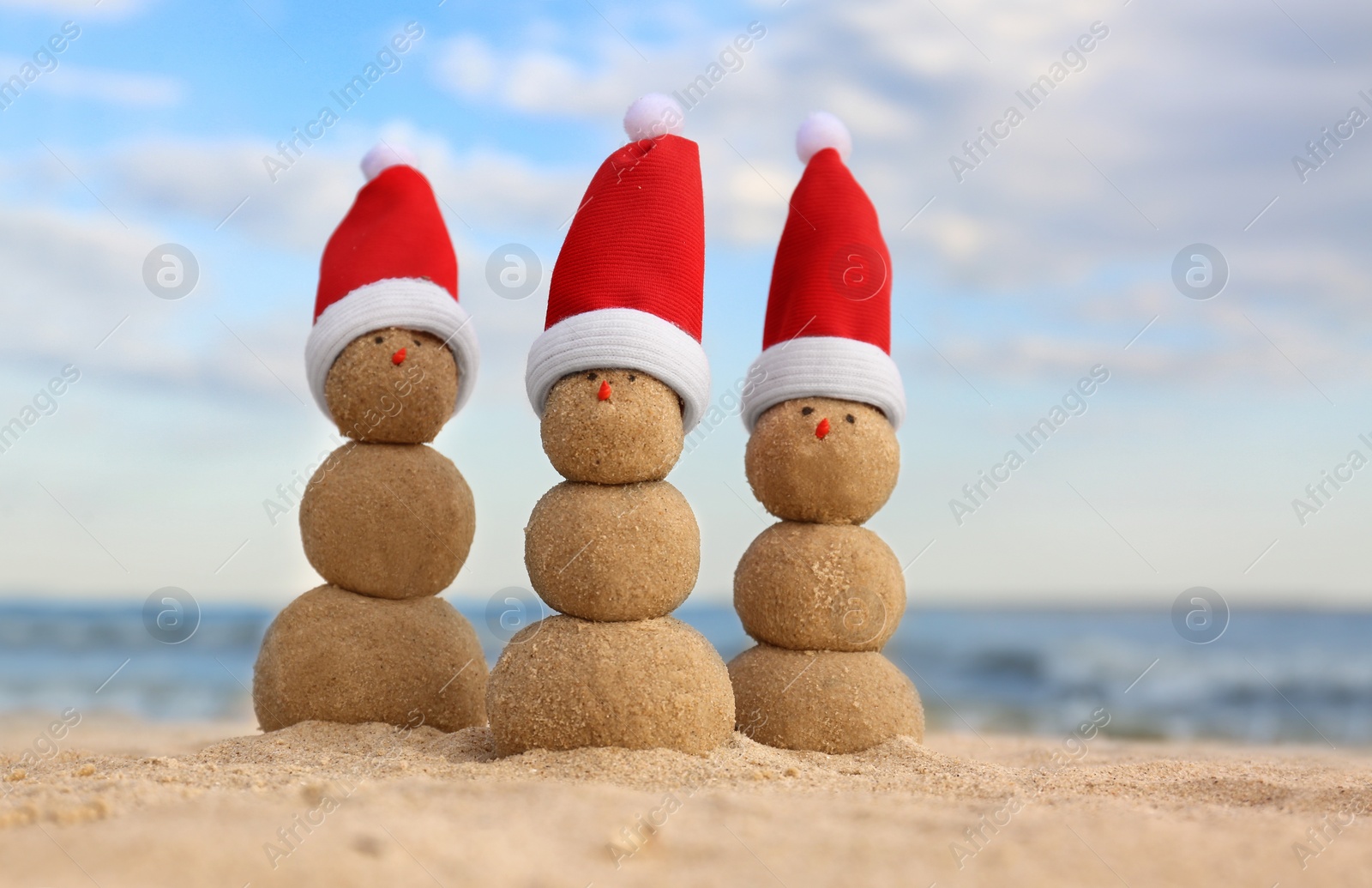 Photo of Snowmen made of sand with Santa hats on beach near sea. Christmas vacation