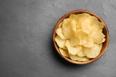 Photo of Bowl of potato chips on grey table, top view. Space for text