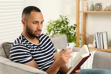 Young man using smartphone while reading book at home. Internet addiction