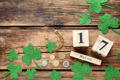 Flat lay composition with clover leaves and block calendar on wooden table, space for text. St. Patrick's Day celebration