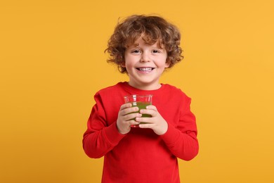 Photo of Cute little boy with glass of fresh juice on orange background