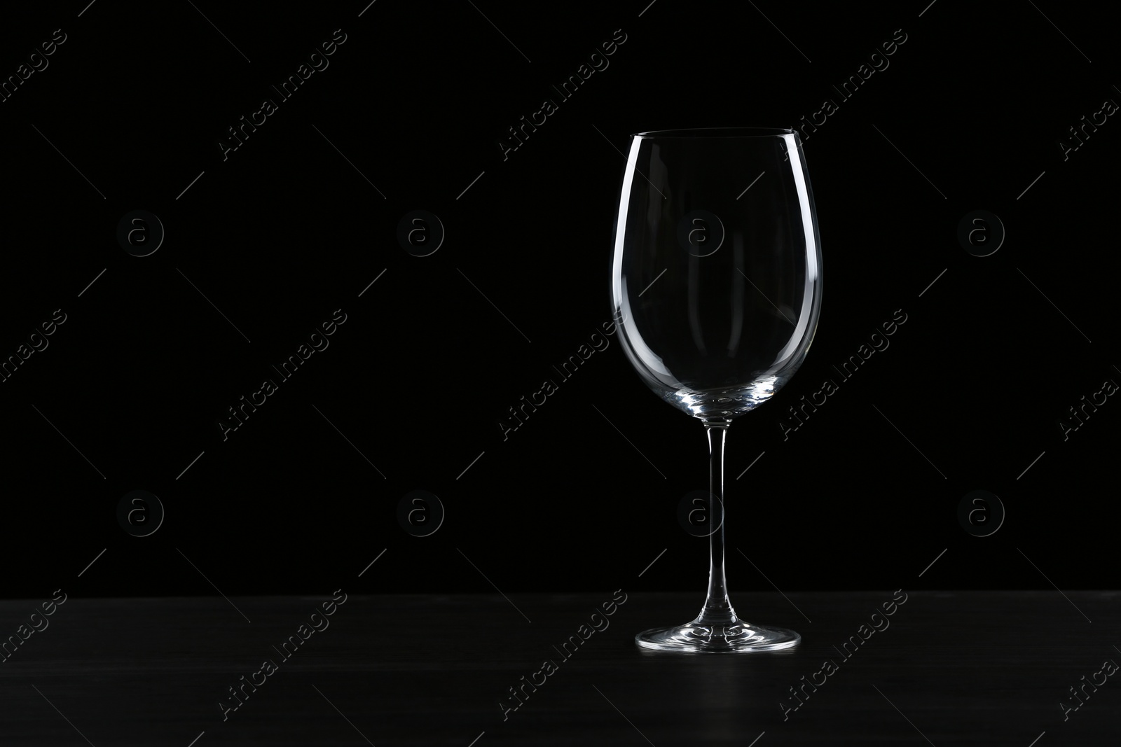 Photo of Empty wine glass on table against black background, space for text