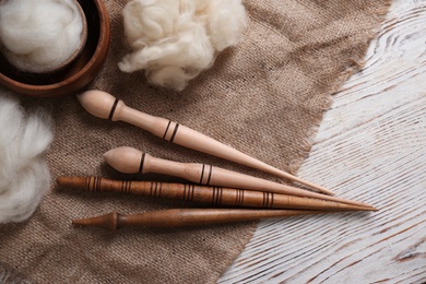 Soft wool and spindles on white wooden table, flat lay