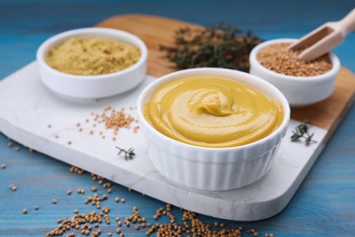 Photo of Delicious mustard and seeds on light blue wooden table, closeup