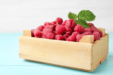 Photo of Crate of delicious fresh ripe raspberries with leaves on blue wooden table