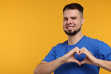 Photo of Man showing heart gesture with hands on golden background. Space for text