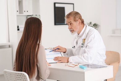 Professional orthopedist consulting patient at table in clinic