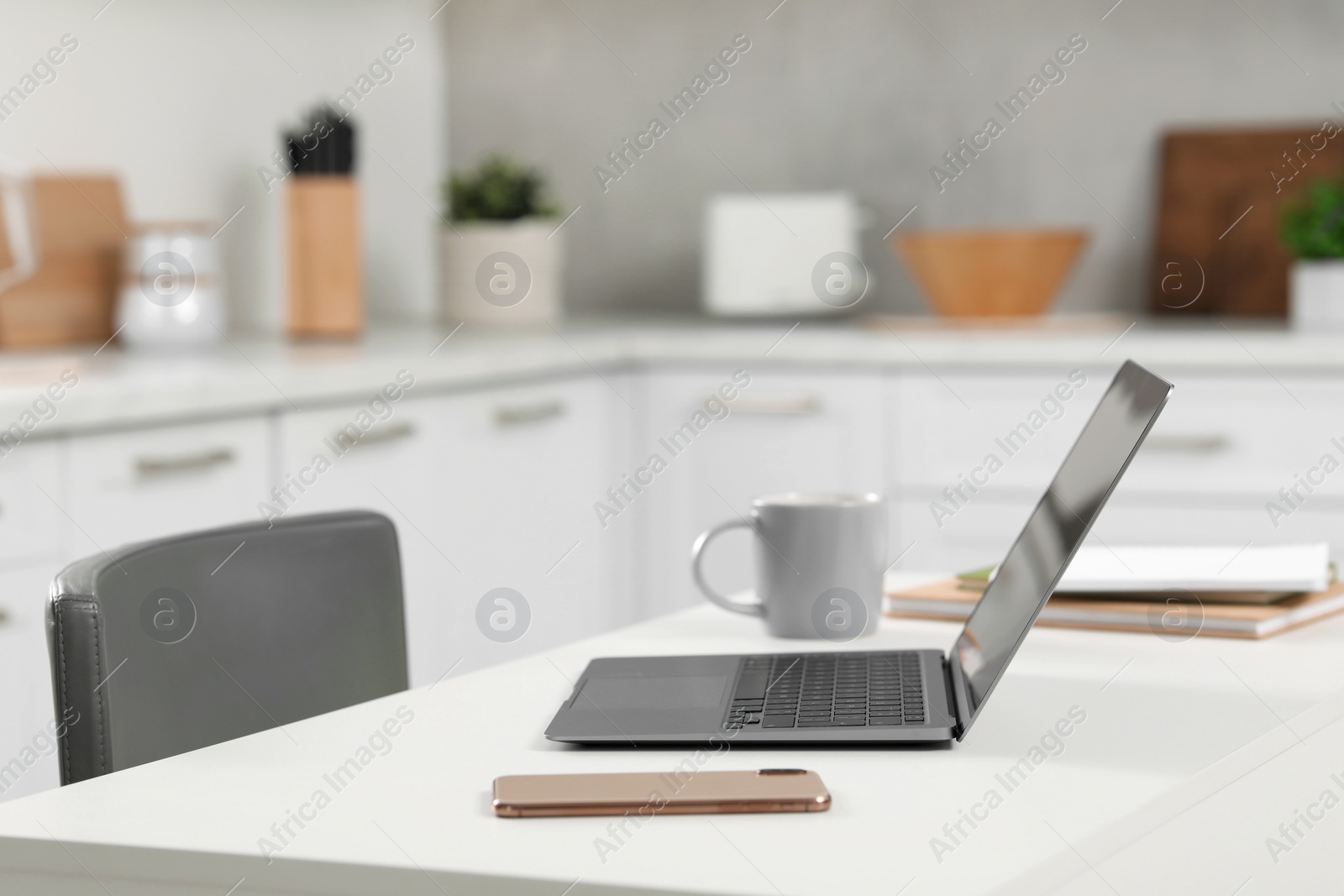 Photo of Home office. Laptop, smartphone, cup and stationery on white desk in kitchen, space for text