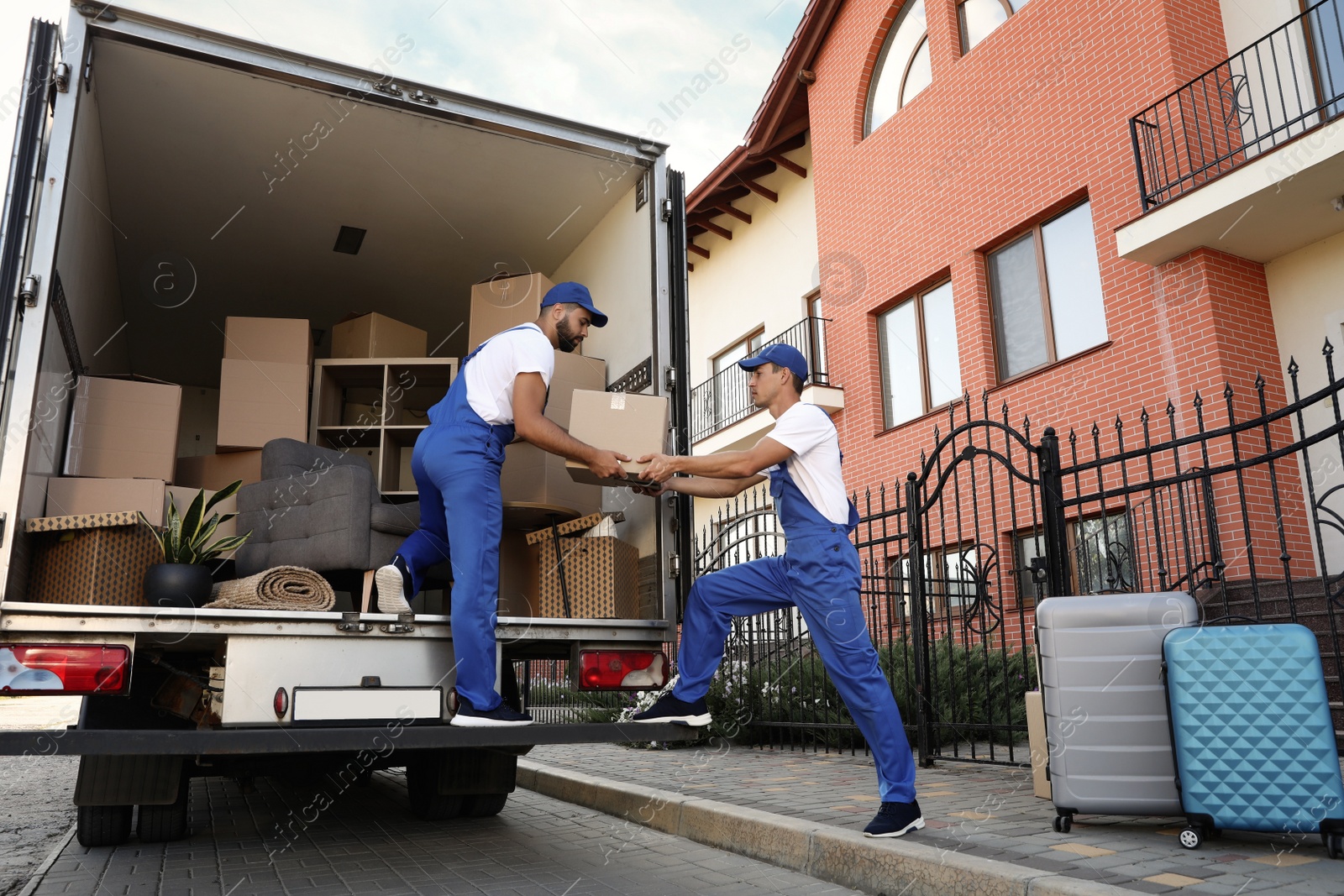 Photo of Workers unloading boxes from van outdoors. Moving service