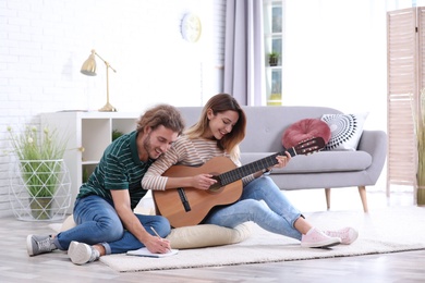 Photo of Young couple playing acoustic guitar and composing song in living room