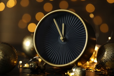 Photo of Stylish clock with decor on black table against blurred Christmas lights, closeup. New Year countdown