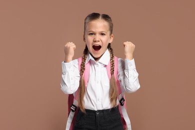 Photo of Emotional schoolgirl with backpack on brown background