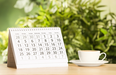 Calendar and cup of coffee on wooden table against blurred background