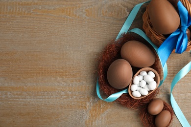 Delicious chocolate Easter eggs and ribbon on wooden table, flat lay. Space for text