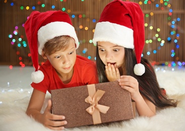 Photo of Cute little children in Santa hats opening Christmas gift box on floor