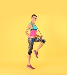 Full length portrait of young sportive woman with jump rope on color background