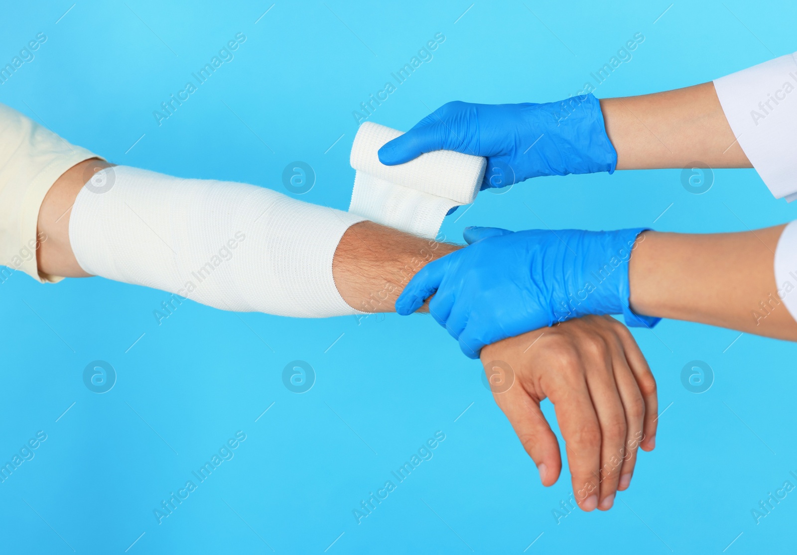 Photo of Doctor applying medical bandage onto patient's arm on light blue background, closeup