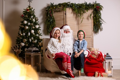 Photo of Santa Claus with little children in photo zone decorated for Christmas
