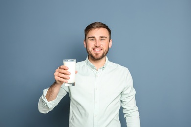 Young man with glass of tasty milk on color background